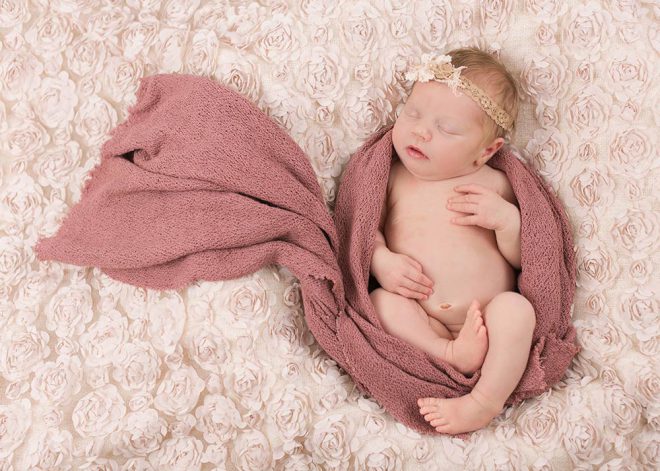 Neugeborenes Mädchen mit Haarband ist in ein Tuch eingewickelt